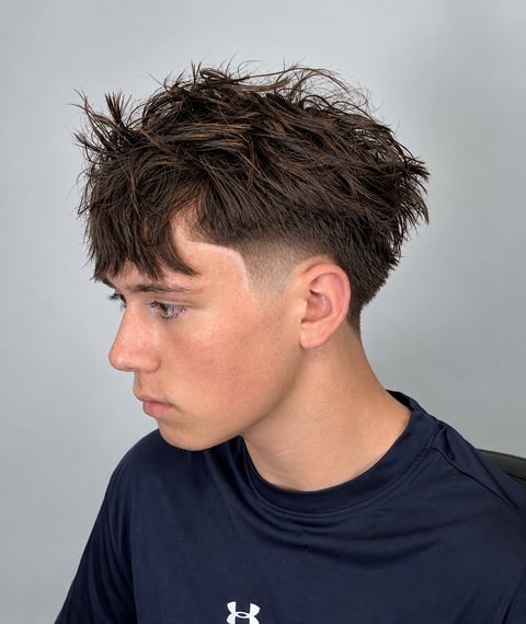 Young man with textured dark brown short hairstyle with fade, wearing navy blue t-shirt, profile view