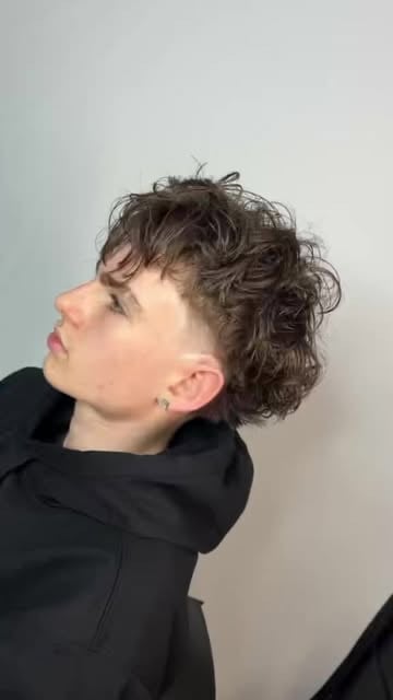Person with curly dark hair wearing a black hoodie, shown in profile view