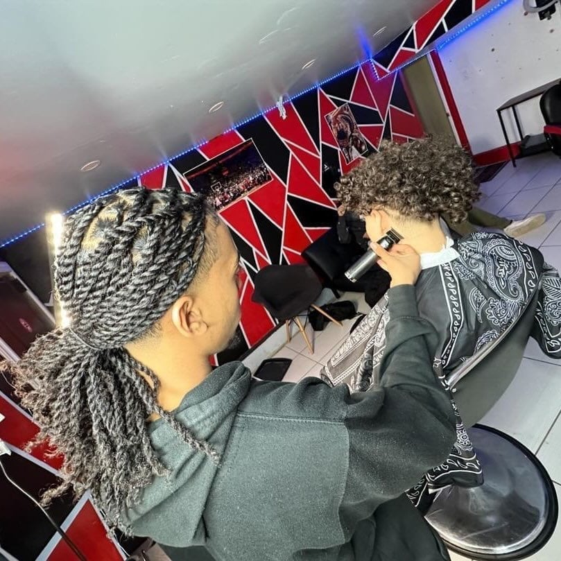 Two people with braided hairstyles holding a camera indoors under red and blue geometric neon signage
