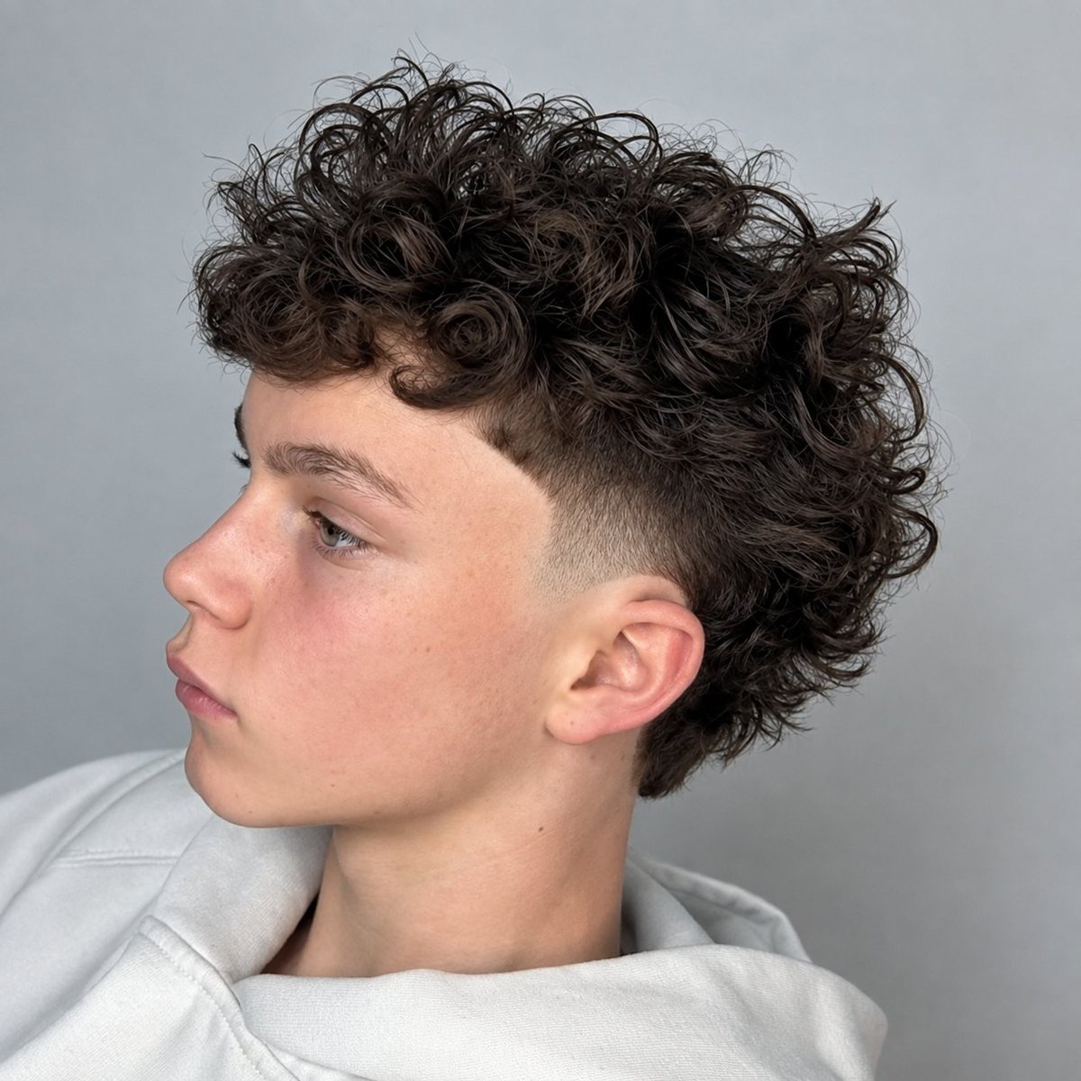 Side profile of a young person with a curly dark hair undercut and faded sides, wearing a light-colored shirt