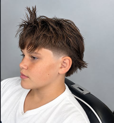 Young person with modern mullet hairstyle featuring shaggy brown hair on top and faded undercut sides, wearing white t-shirt, profile view