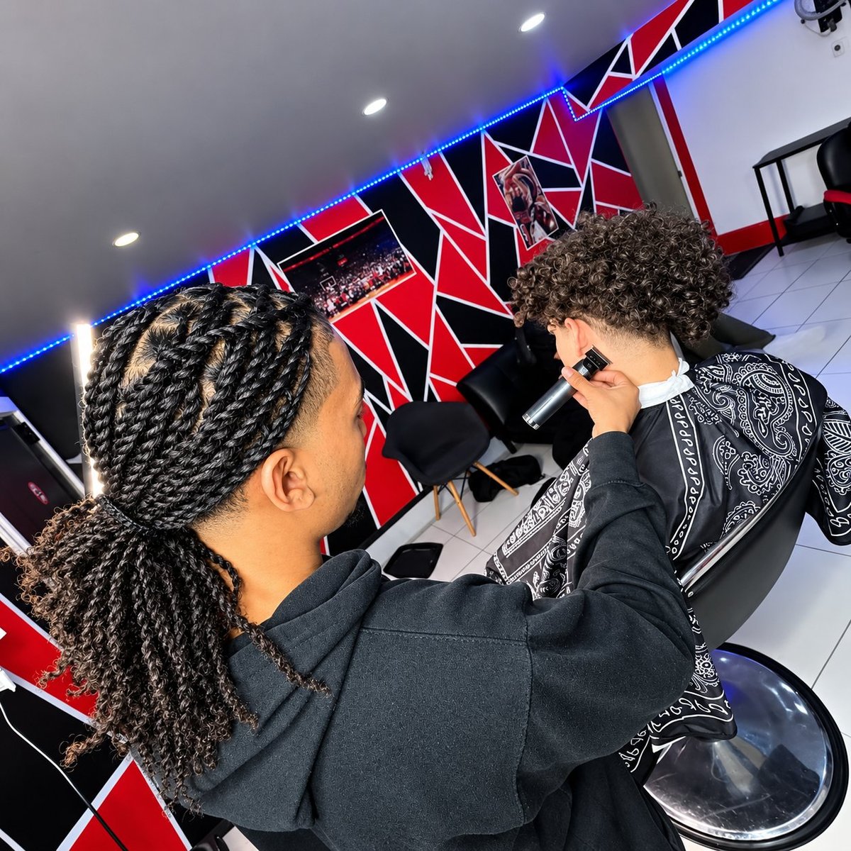 Two people operating film cameras in a modern studio with red and blue geometric backdrop signage and white ceiling