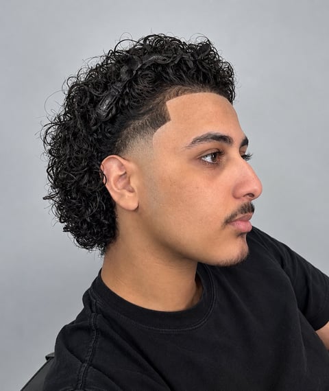 Man with curly black hair in profile wearing a black shirt against a gray background